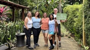 Group of people standing on a path flanked by lush tropical foliage holding a green sign that reads: Welcome to Entreprenew